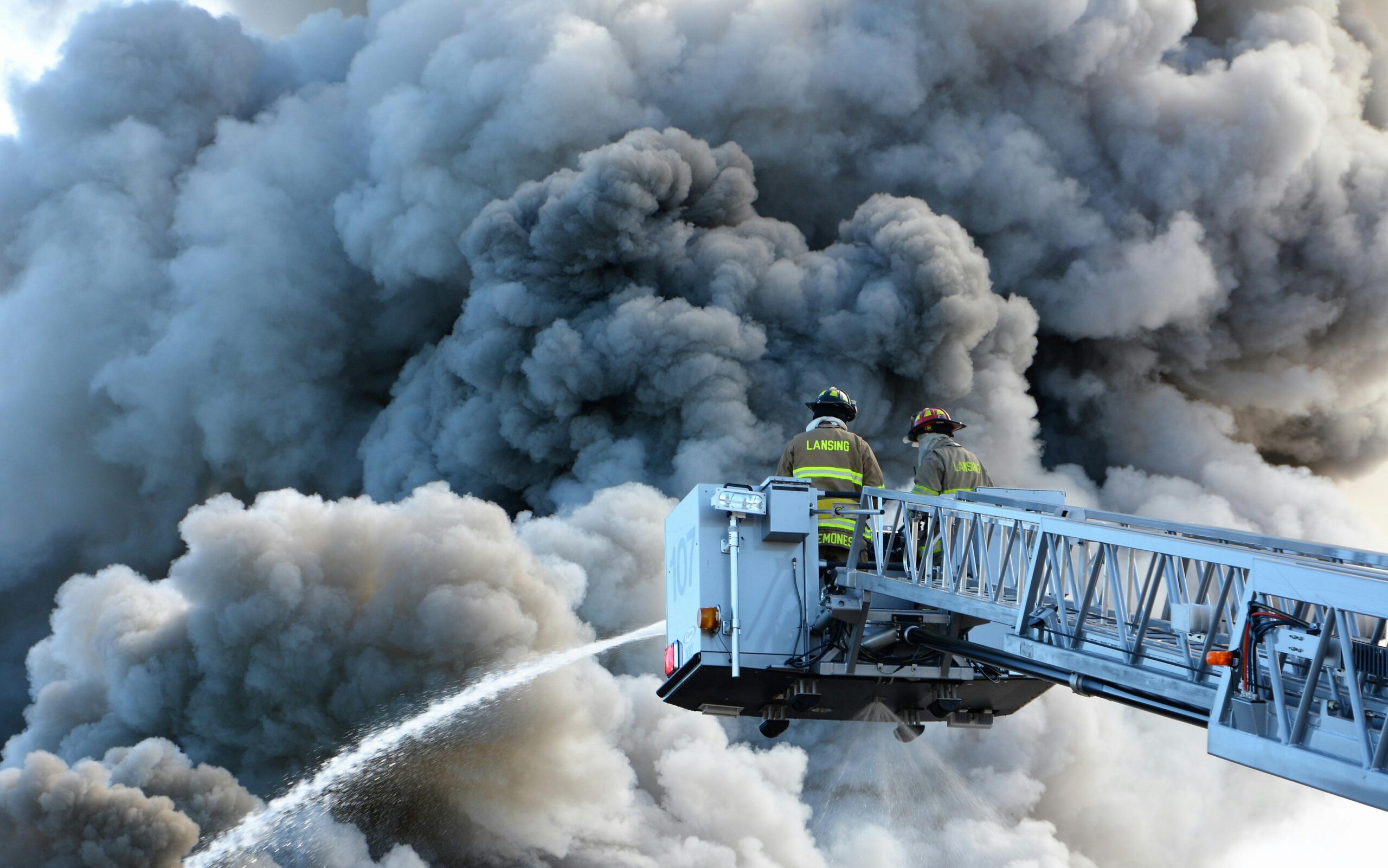 Firefighters on an aerial ladder battling dense smoke clouds during a fire emergency.